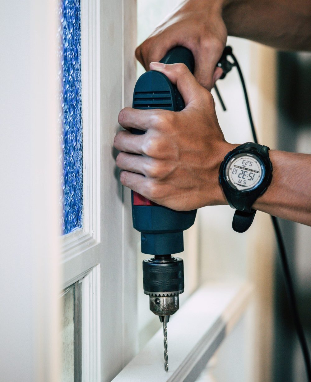 The carpenter holds the drill and drills the window. Selective focus.